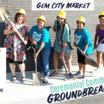 Five Gem City Market Members in plastic hard hats with shovels outside a building. Words on photo tell us it's an invitation to the GCM Community Groundbreaking event on Sept 18th from 4pm to 8pm